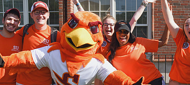 Benny Hawk mascot and students clad in orange cheer and smile for the camera.