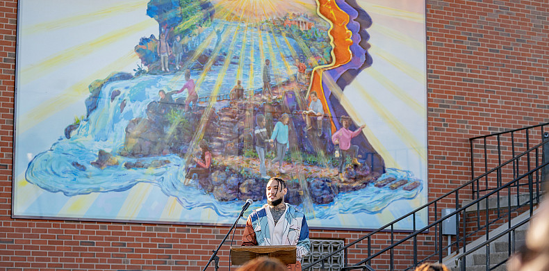 Man stands at podium in front of a vibrant mural.