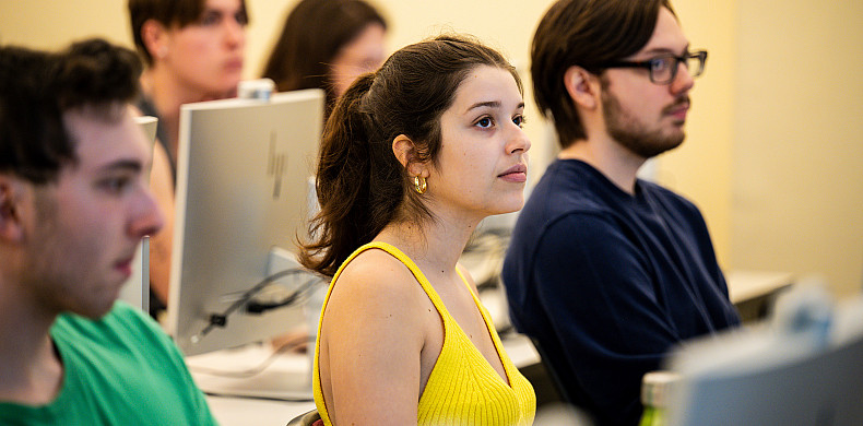 Students sit in front of computers in a classroom.